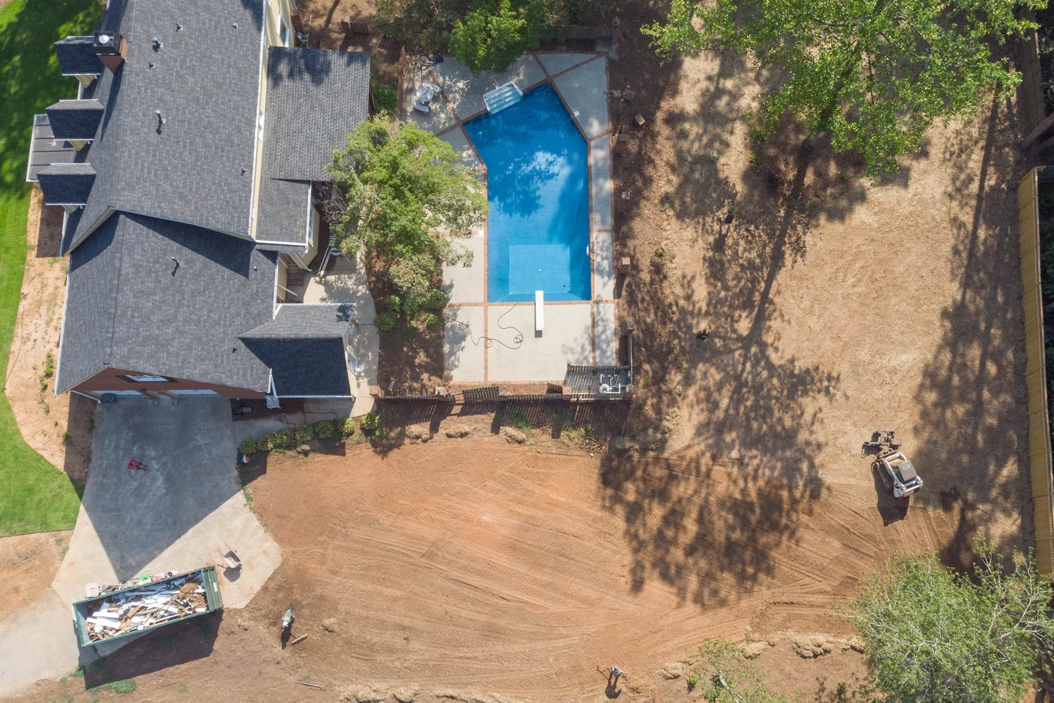 Before: aerial view of a backyard graded to bare soil with a skid steer at work
