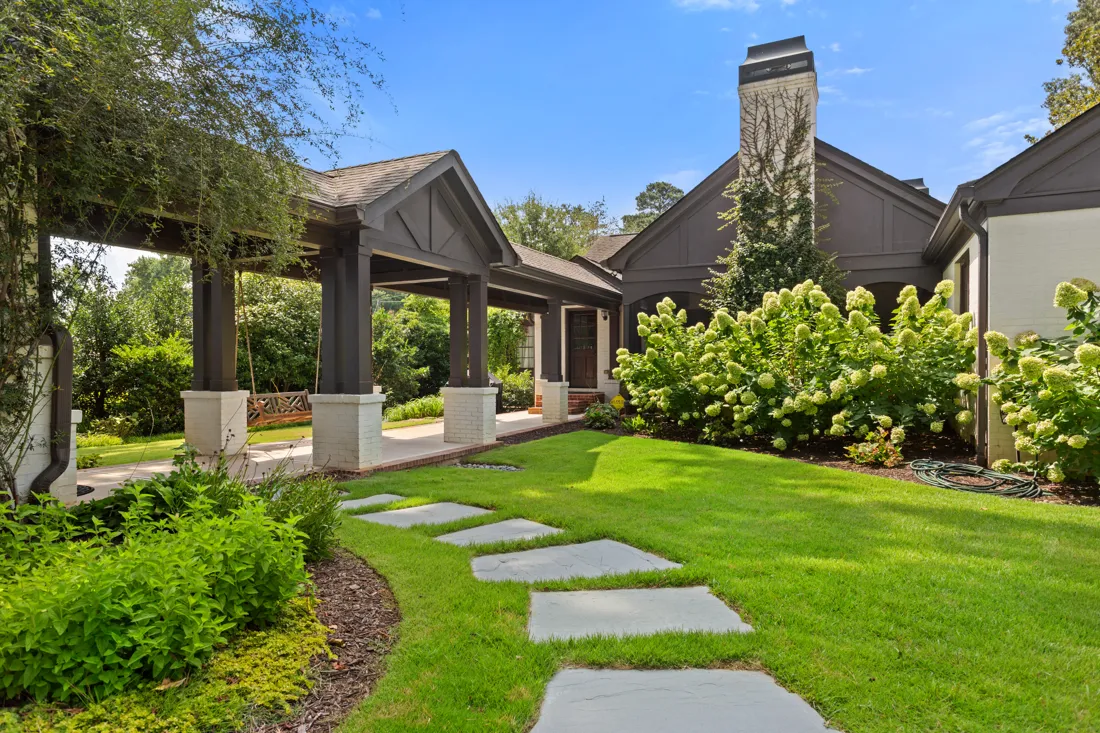 Stepping stones across a lawn to a covered pavilion beside blooming hydrangeas